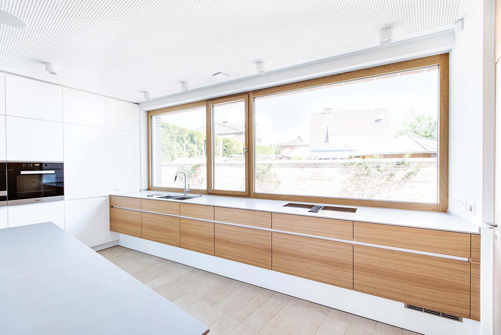 Große Fensterfront bietet Ausblick aus der Design Küche ins Grüne. Natureiche gepaart mit weiß macht diese geradlinige Küche modern und zum Design Objekt.